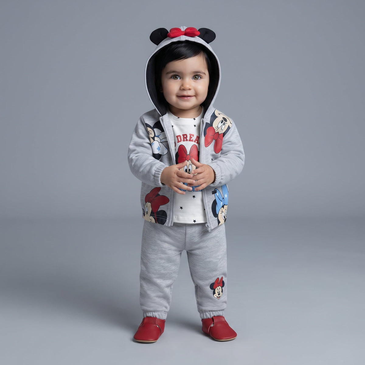 Bebé con conjunto EmpiBy de 3 piezas Minnie Mouse: chaqueta gris con orejas, camiseta blanca y pantalón jogger gris.