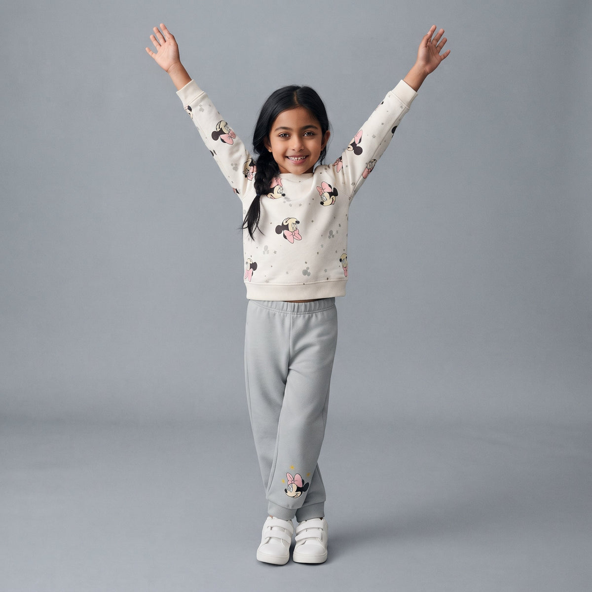 Niña sonriente con conjunto EmpiBy de sudadera blanca estampada de Minnie Mouse y pantalón jogger gris cómodo.