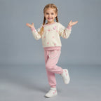 Niña sonriente vistiendo conjunto EmpiBy de dos piezas crema y rosa con estampado de corazones, volantes y lazos