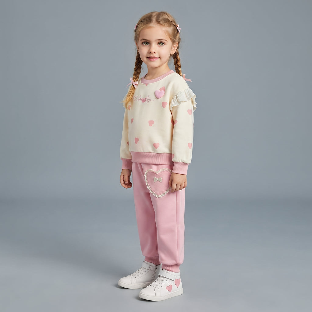 Niña con conjunto EmpiBy de dos piezas: sudadera crema con corazones rosas y pantalón rosa con bolsillo de corazón.