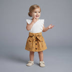 Niña pequeña vistiendo conjunto EmpiBy de falda mostaza con flores y camiseta blanca con volantes en los hombros