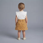 Vista trasera de niña con conjunto EmpiBy de falda de pana mostaza con flores y camiseta blanca con volantes
