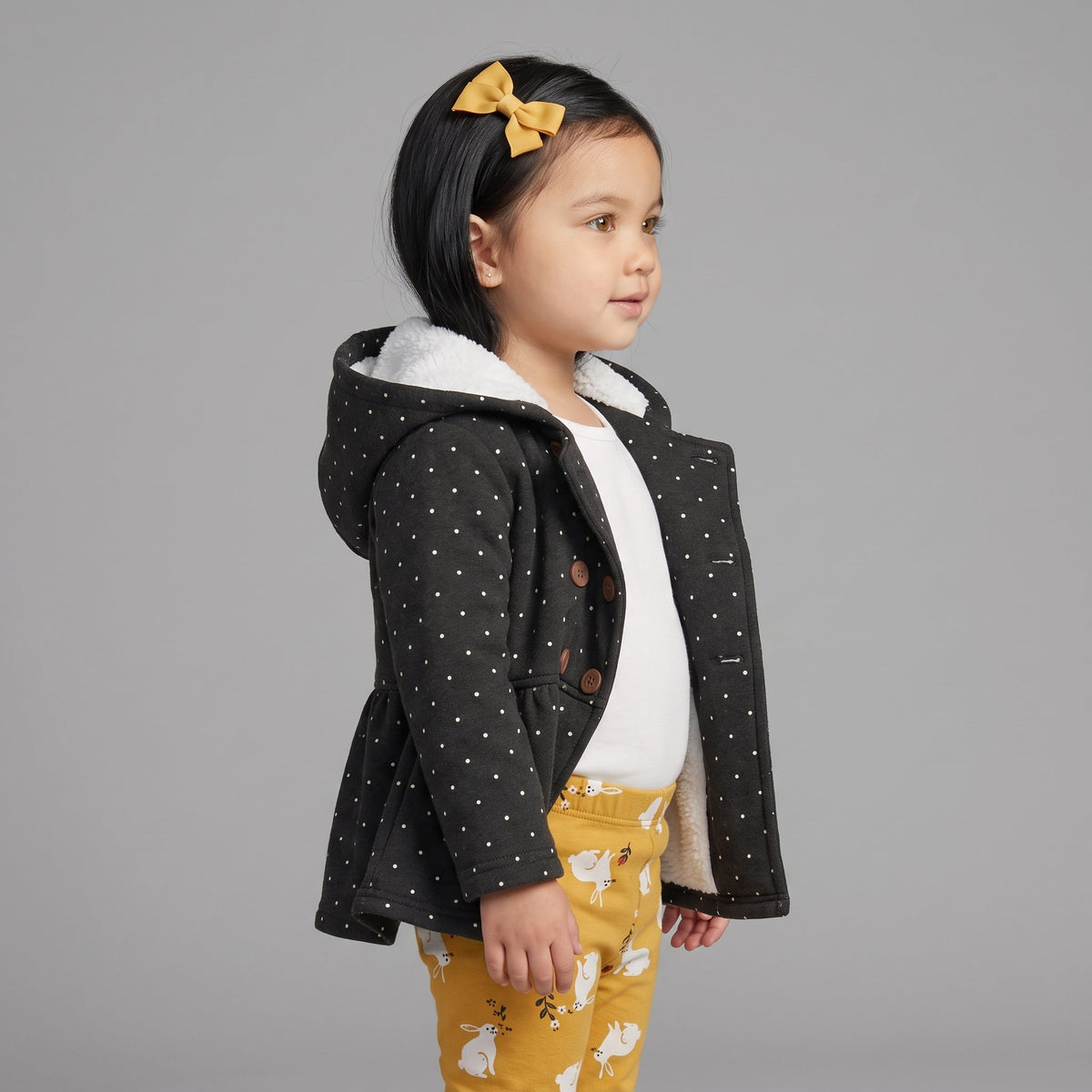 Conjunto EmpiBy de 3 piezas para niña: chaqueta negra con lunares, body blanco y pantalón mostaza con conejitos.