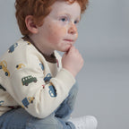 Niño pelirrojo con conjunto EmpiBy de suéter crema estampado de carritos y jeans de mezclilla azul claro