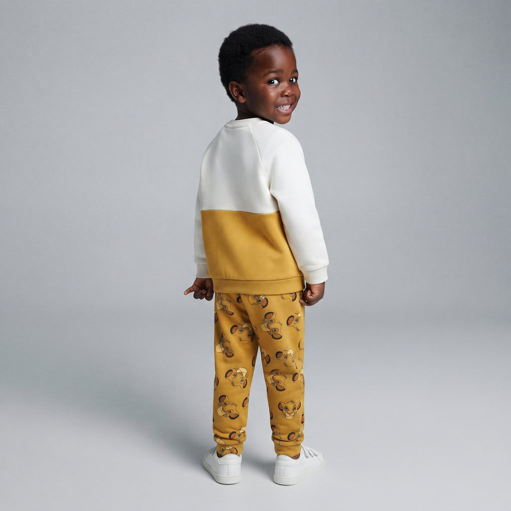 Niño vistiendo conjunto EmpiBy de El Rey León con sudadera color-blocked crema y mostaza y jogger estampado de Simba