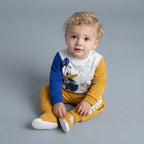Bebé con conjunto EmpiBy de dos piezas del Pato Donald, sudadera mostaza y azul con jogger a juego en fondo gris.