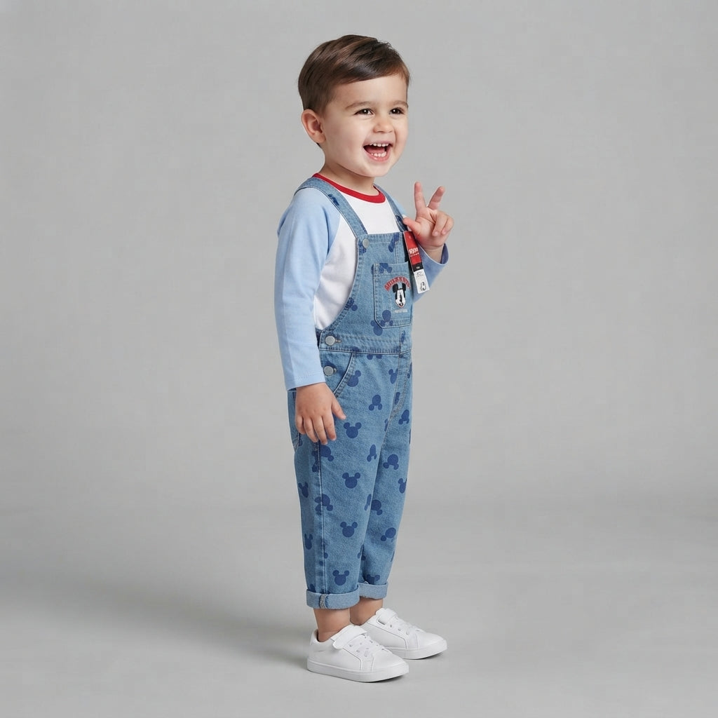 Niño sonriente vistiendo conjunto EmpiBy de peto vaquero con estampado de Mickey Mouse y camiseta de manga larga.
