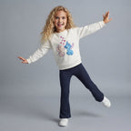 Niña sonriente vistiendo conjunto EmpiBy de sudadera color hueso con estampado de Stitch y Angel y pantalón azul marino