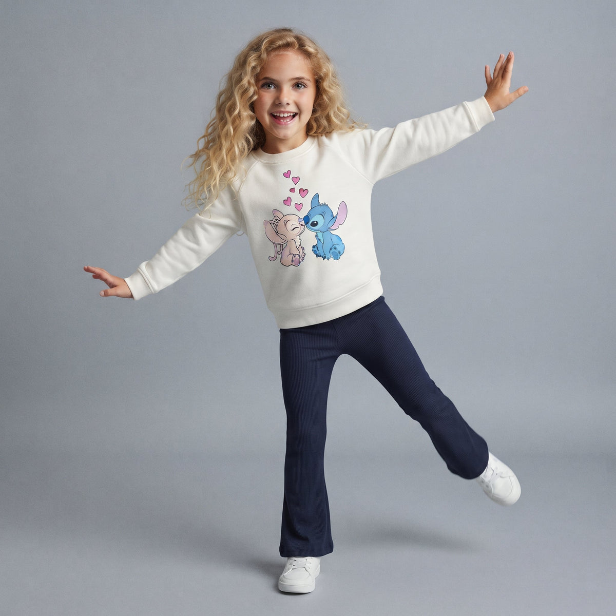 Niña sonriente vistiendo conjunto EmpiBy de sudadera color hueso con estampado de Stitch y Angel y pantalón azul marino