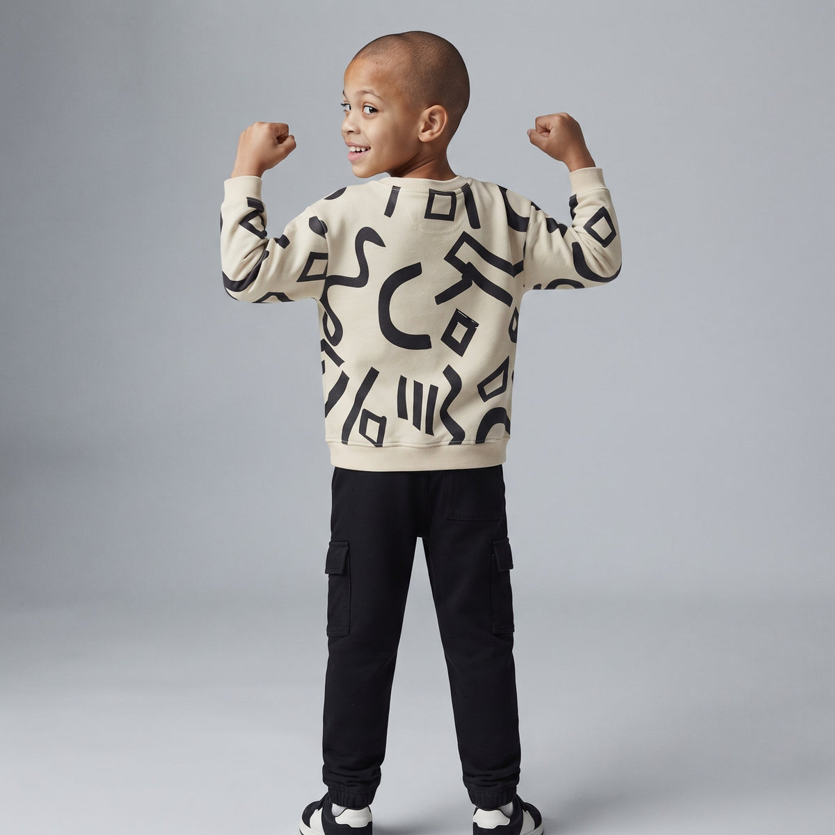Niño posando de espaldas con conjunto EmpiBy de sudadera marfil con estampado abstracto negro y pantalón jogger cargo