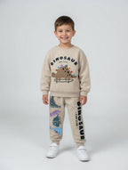 Niño sonriente vistiendo conjunto EmpiBy beige de sudadera y pantalón con estampado de dinosaurios skaters