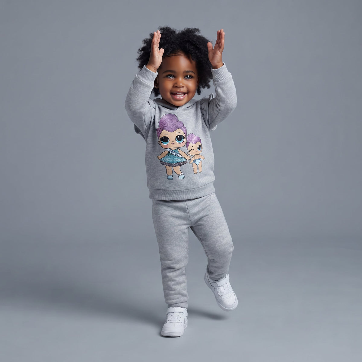Niña pequeña sonriente vistiendo conjunto EmpiBy gris de dos piezas con sudadera de muñecas y pantalón jogger
