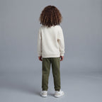 Vista trasera de niño con conjunto EmpiBy de sudadera marfil y pantalón jogger verde oliva sobre fondo gris