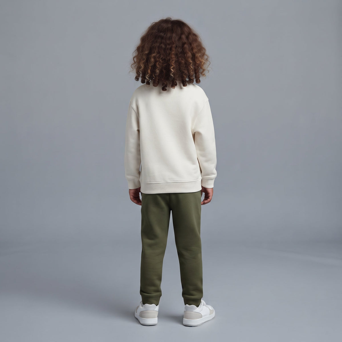 Vista trasera de niño con conjunto EmpiBy de sudadera marfil y pantalón jogger verde oliva sobre fondo gris