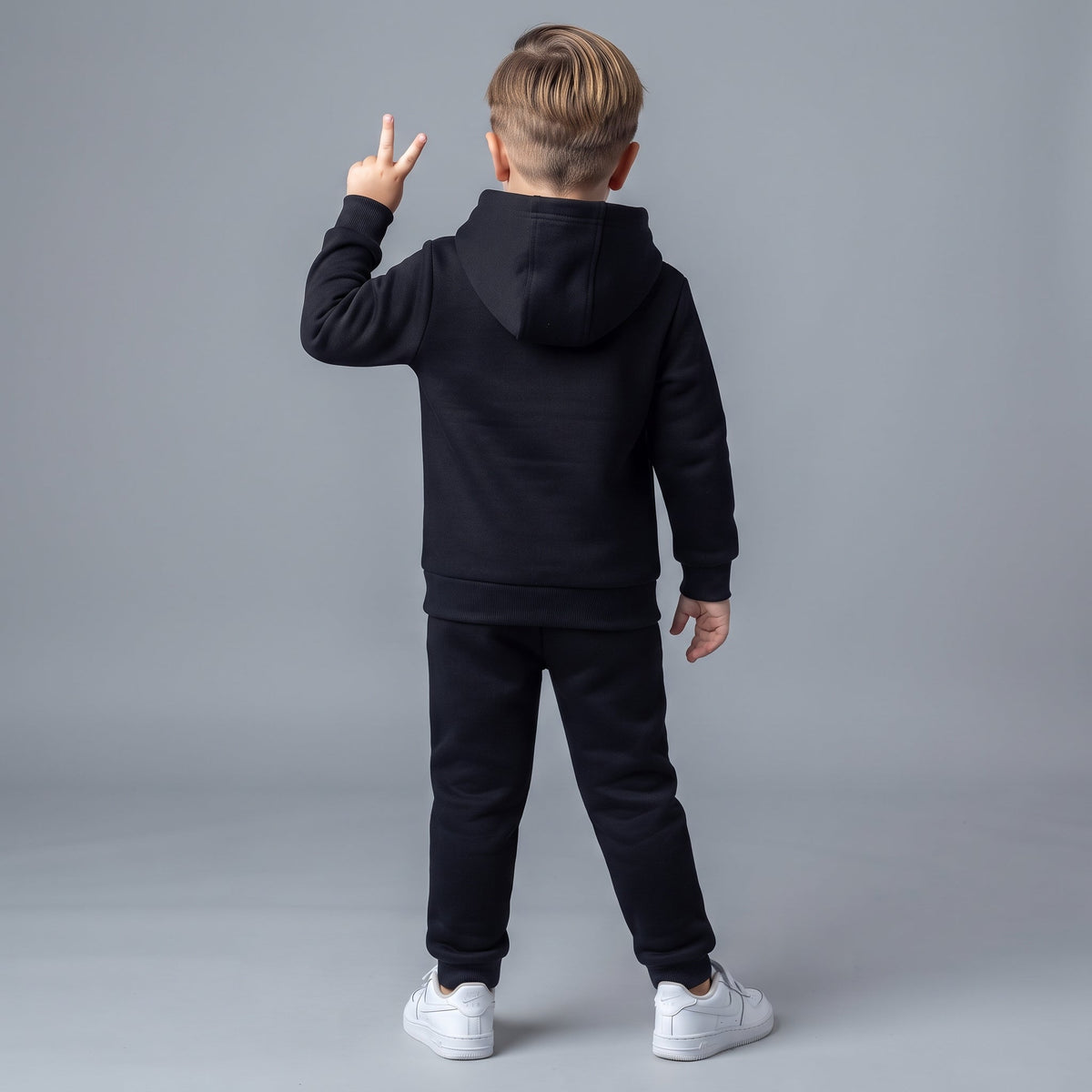 Niño de espaldas vistiendo conjunto EmpiBy de sudadera con capucha y pantalón jogger negro, estilo deportivo casual.