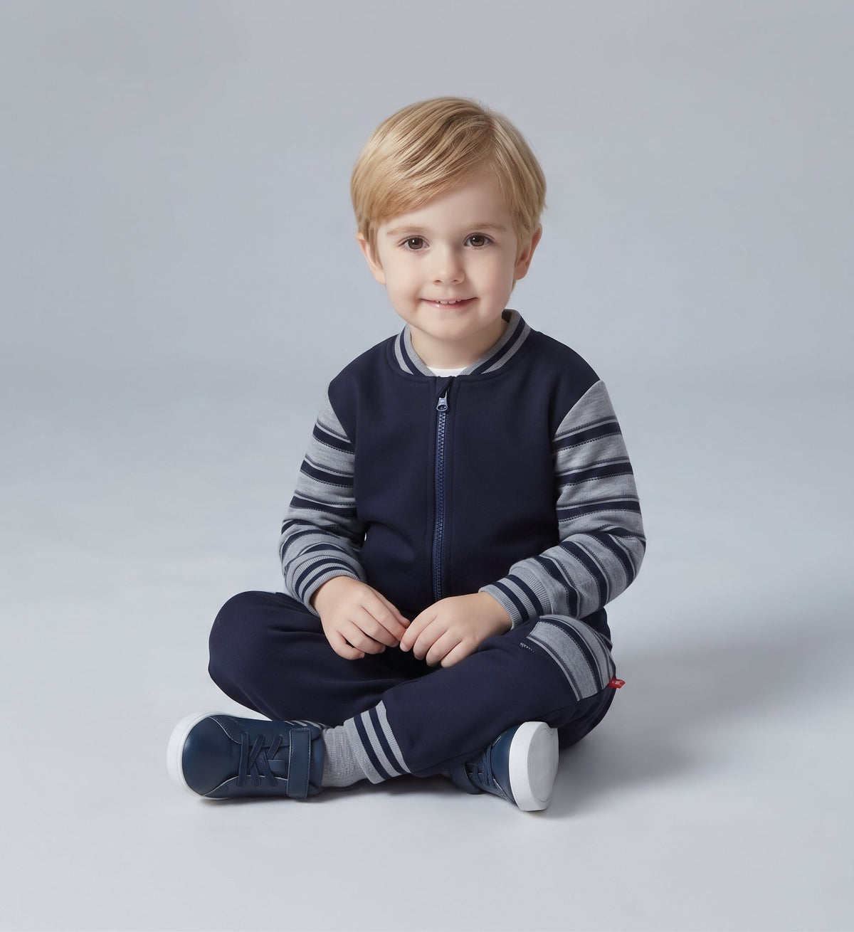 Niño pequeño sentado vistiendo conjunto EmpiBy de chaqueta bomber azul marino y gris con pantalón a juego