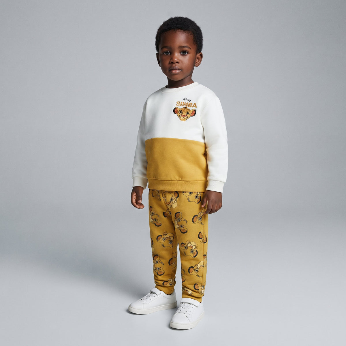 Niño vistiendo conjunto EmpiBy de El Rey León con sudadera color-blocked crema y mostaza y jogger estampado de Simba