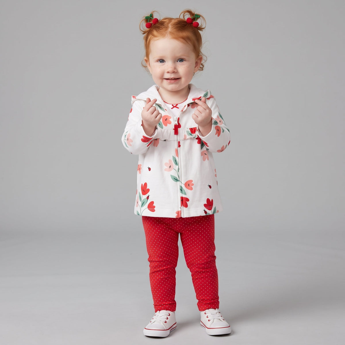 Niña pequeña con conjunto EmpiBy de tres piezas: chaqueta blanca con flores, body y leggings rojos de lunares.