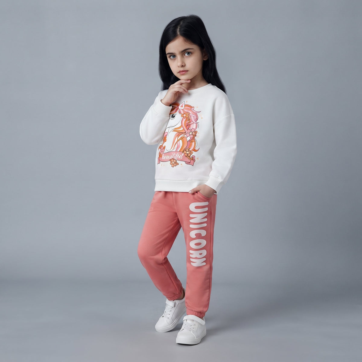 Niña vistiendo conjunto EmpiBy de sudadera crudo con estampado de unicornio y pantalón jogger coral con texto lateral