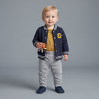 Bebé con conjunto EmpiBy de 3 piezas: chaqueta universitaria azul, body naranja estampado y pantalón gris cómodo.