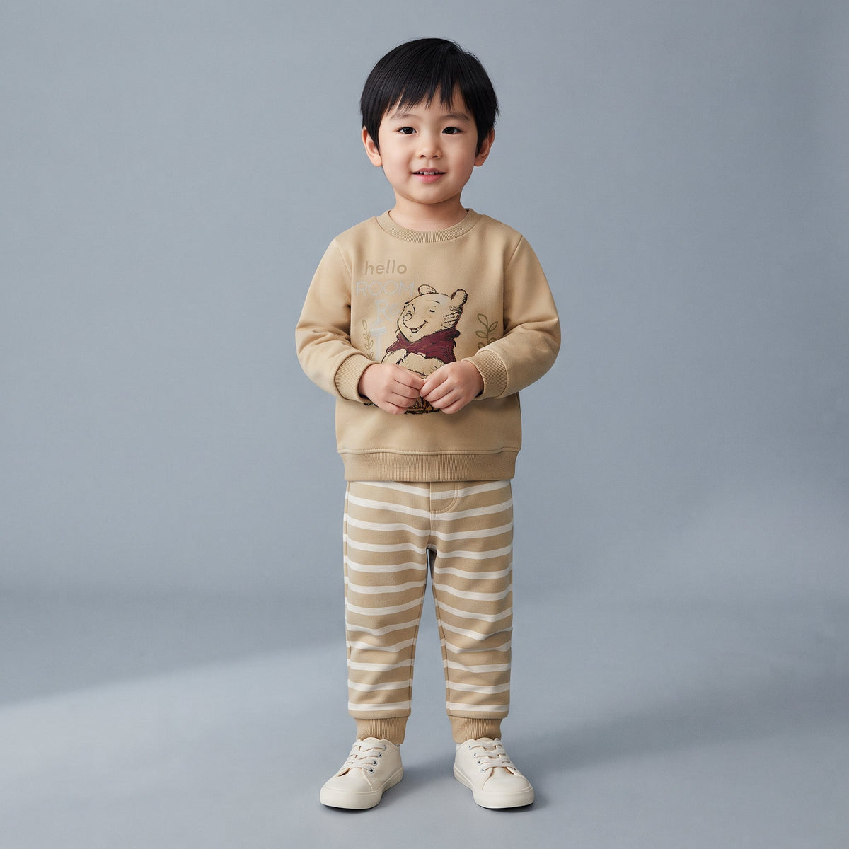 Niño vistiendo conjunto de dos piezas EmpiBy de Winnie the Pooh con sudadera beige y pantalón jogger a rayas