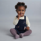 Bebé niña sonriente vistiendo overol EmpiBy azul marino con bordado de conejito y camiseta de manga larga crema
