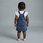 Bebé niña vistiendo un overol de mezclilla EmpiBy con bordados florales y camisa blanca con volados, vista trasera.
