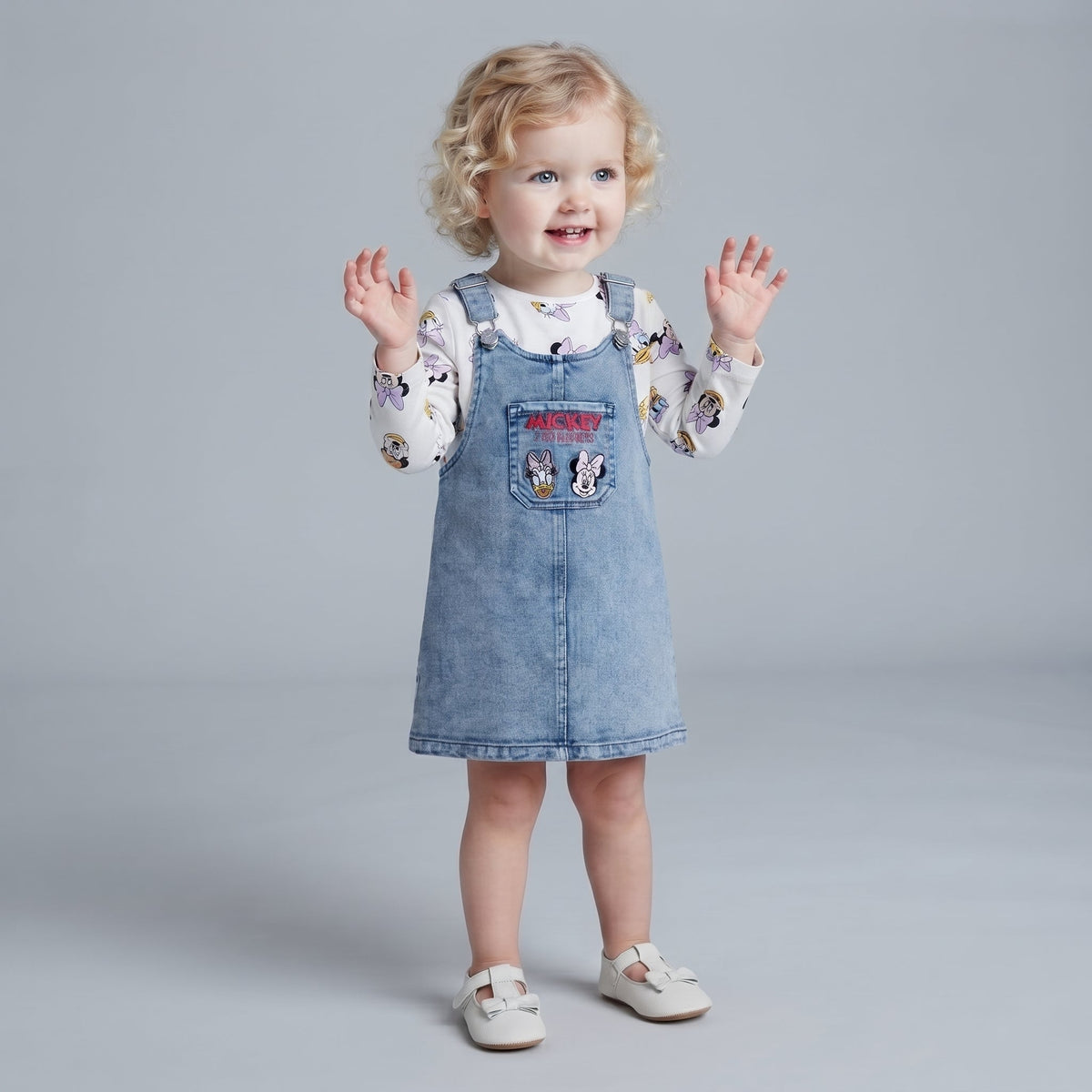 Niña pequeña con vestido overol de mezclilla EmpiBy y camiseta blanca de manga larga con estampado de Minnie Mouse