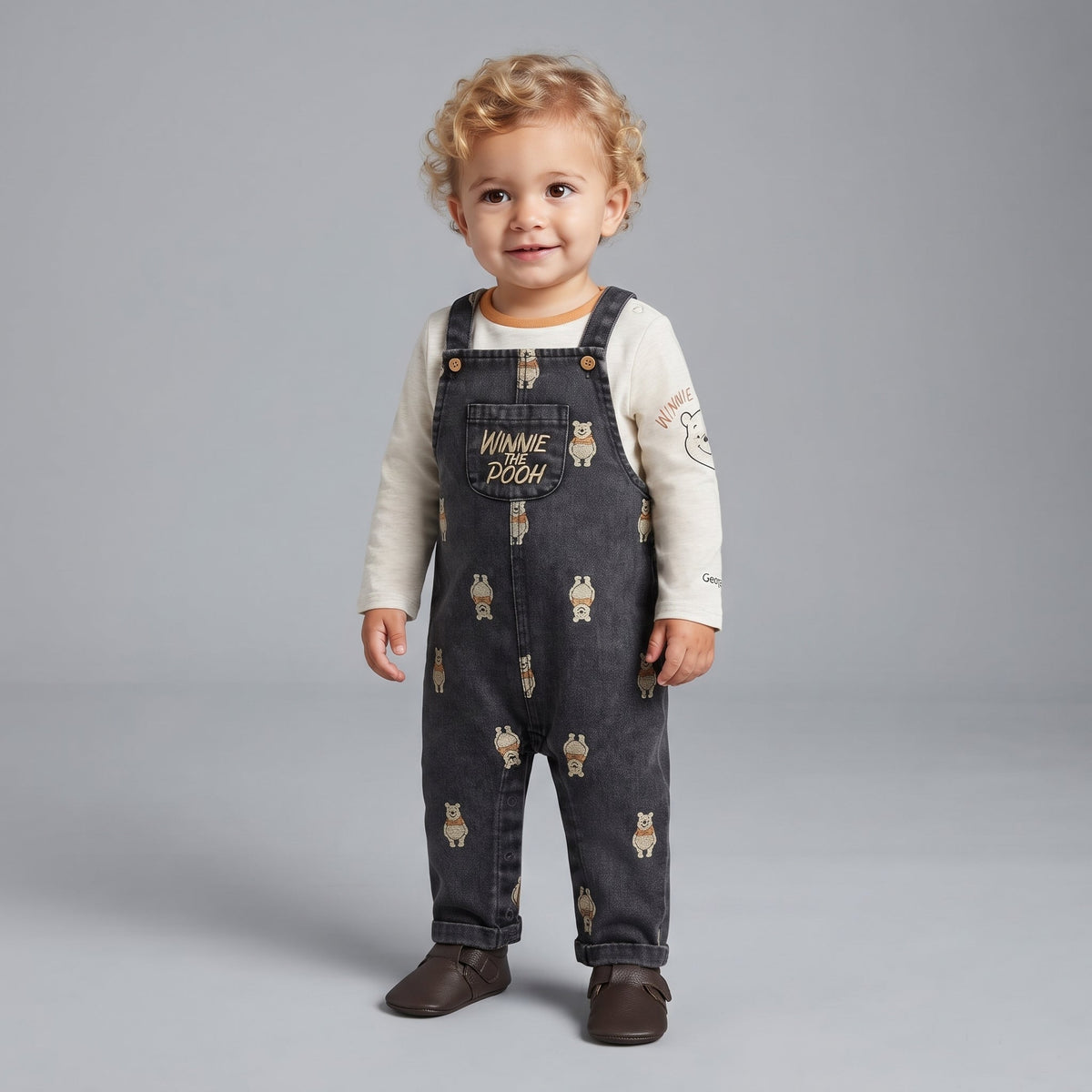 Bebé niño vistiendo overol de mezclilla oscura EmpiBy con estampado de Winnie Pooh y camiseta beige de manga larga