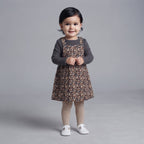 Niña pequeña con conjunto EmpiBy de vestido tipo peto estampado de leopardo, camiseta gris acanalada y medias beige.