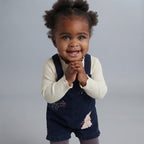 Bebé niña sonriente vistiendo overol EmpiBy azul marino de pana con bordado de conejito y camiseta de canalé crema