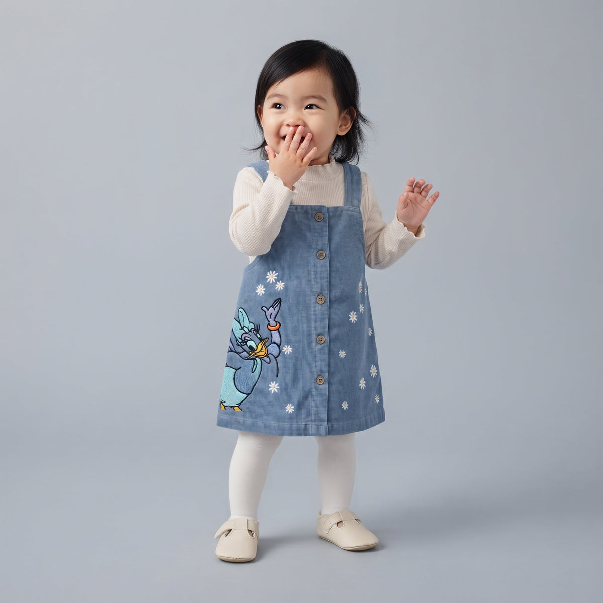 Niña pequeña vistiendo conjunto EmpiBy de 3 piezas: vestido de pana azul con Daisy Duck, camiseta blanca y medias.
