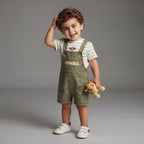 Niño pequeño sonriente con conjunto EmpiBy de overol verde oliva de Simba y camiseta a rayas con parche de león