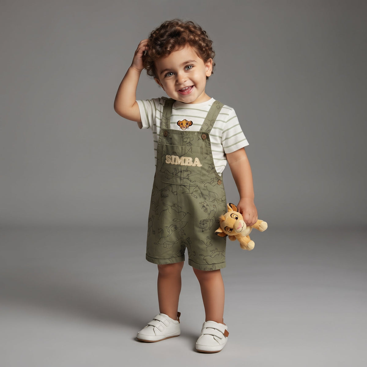 Niño pequeño sonriente con conjunto EmpiBy de overol verde oliva de Simba y camiseta a rayas con parche de león