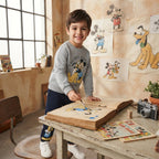 Niño con pantalón de chándal azul marino EmpiBy y gráfico de Mickey Mouse, pintando en un libro en un estudio artístico.