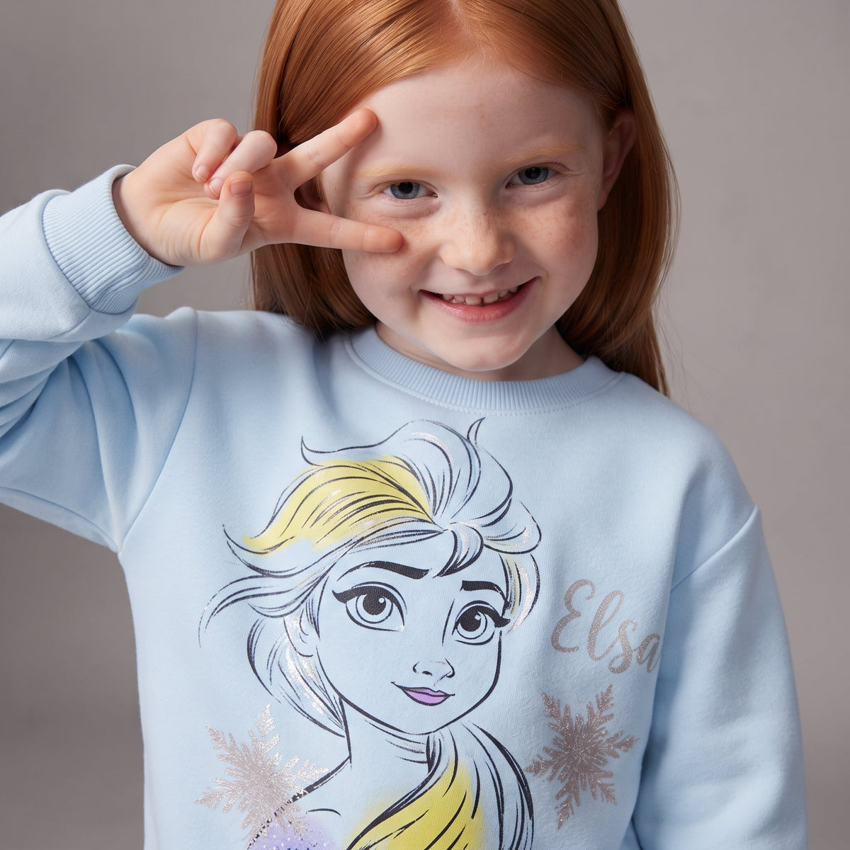 Niña pelirroja sonriendo con sudadera azul claro EmpiBy con estampado de Elsa y detalles brillantes de copos de nieve