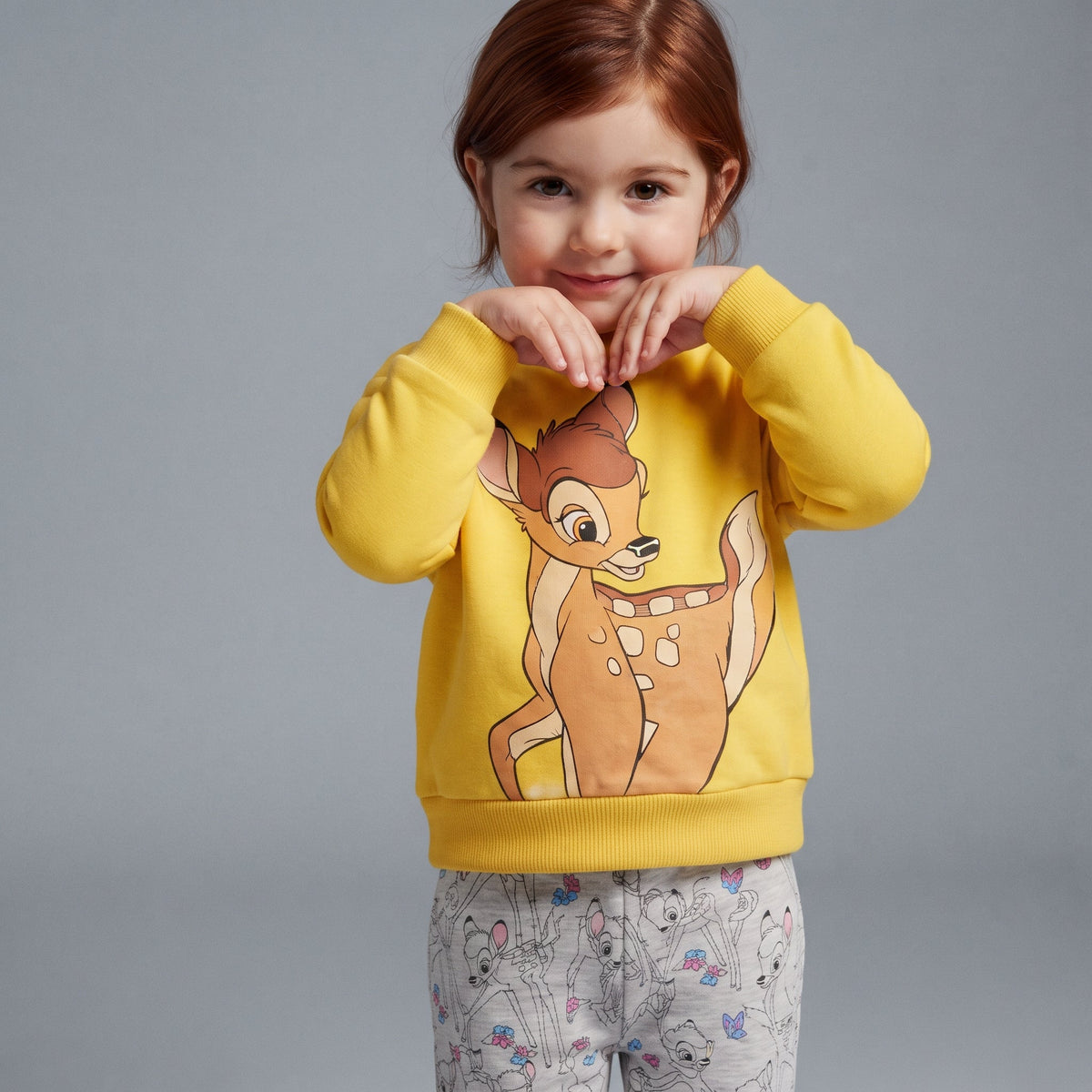 Niña con conjunto EmpiBy de sudadera amarilla de Bambi y pantalón jogger gris estampado con motivos de Disney