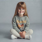 Niña sentada con conjunto EmpiBy de dos piezas: sudadera verde salvia con estampado de Bambi y pantalón jogger gris.