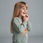 Niña sonriente vistiendo sudadera verde salvia de Bambi de EmpiBy con estampado de personajes Disney