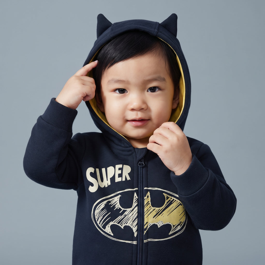Bebé con sudadera EmpiBy de Batman azul marino con capucha, orejas de murciélago y detalles en amarillo vibrante.