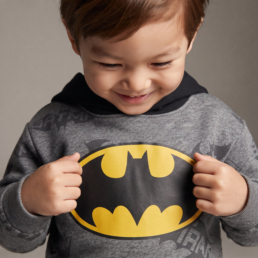Niño sonriente vistiendo sudadera gris EmpiBy con capucha y logo de Batman en amarillo y negro