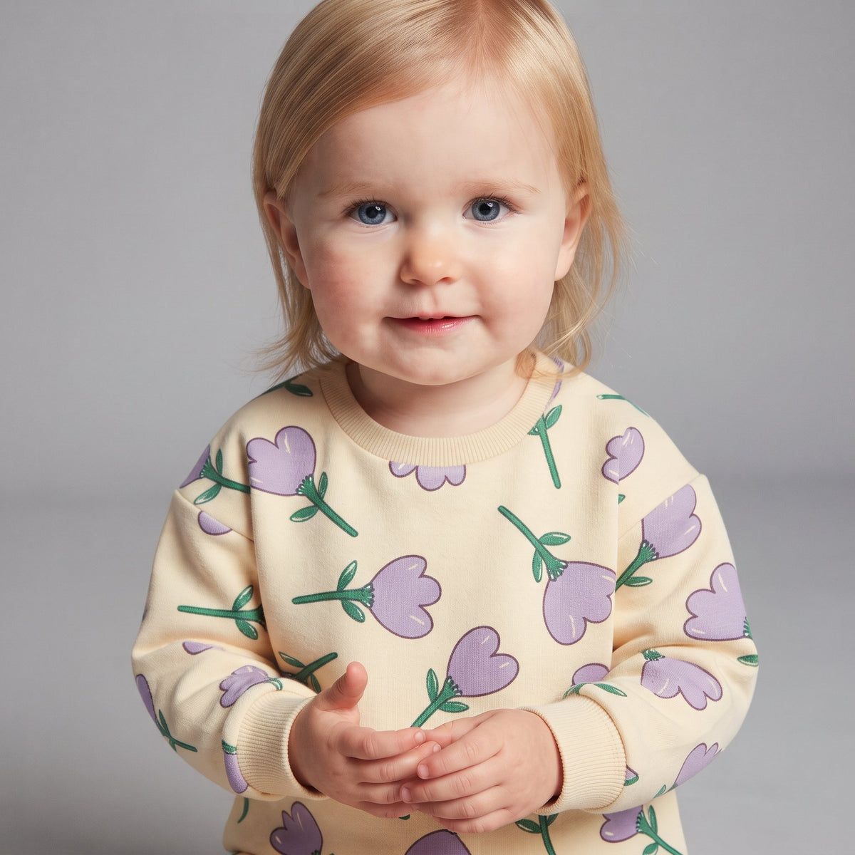 Bebé con sudadera EmpiBy color crema con estampado de tulipanes morados y hojas verdes sobre fondo gris