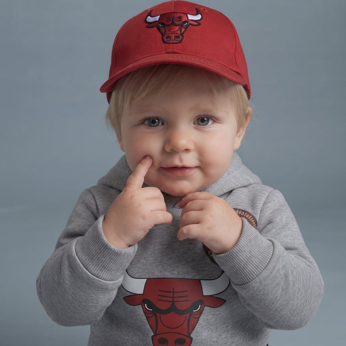 Bebé con sudadera gris EmpiBy de Chicago Bulls y gorra roja, diseño deportivo con gráfico de toro y capucha suave.