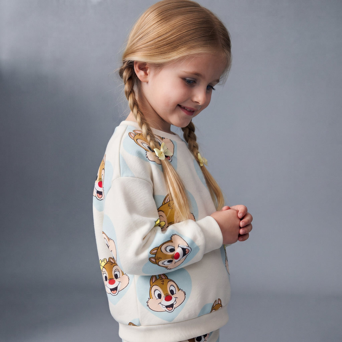 Niña con trenzas vistiendo sudadera EmpiBy de Chip y Dale con estampado de corazones celestes sobre fondo claro