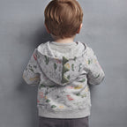 Niño de espaldas vistiendo chaqueta gris con capucha de dinosaurio y estampado colorido de EmpiBy