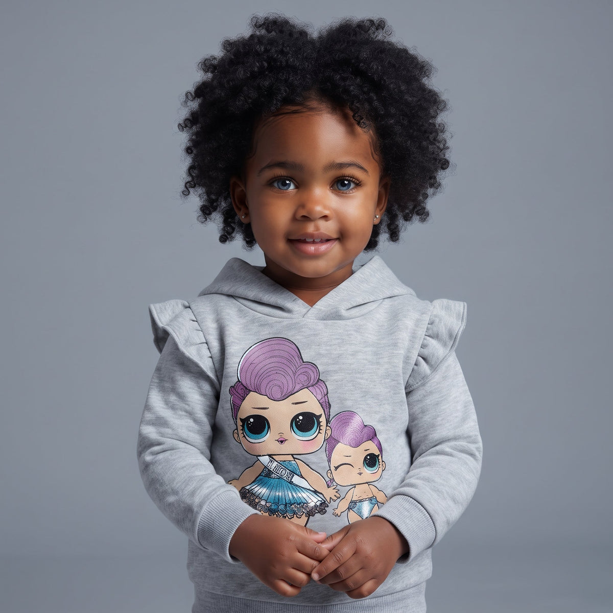 Niña pequeña con sudadera gris EmpiBy con capucha, volantes en hombros y estampado de muñecas estilo LOL