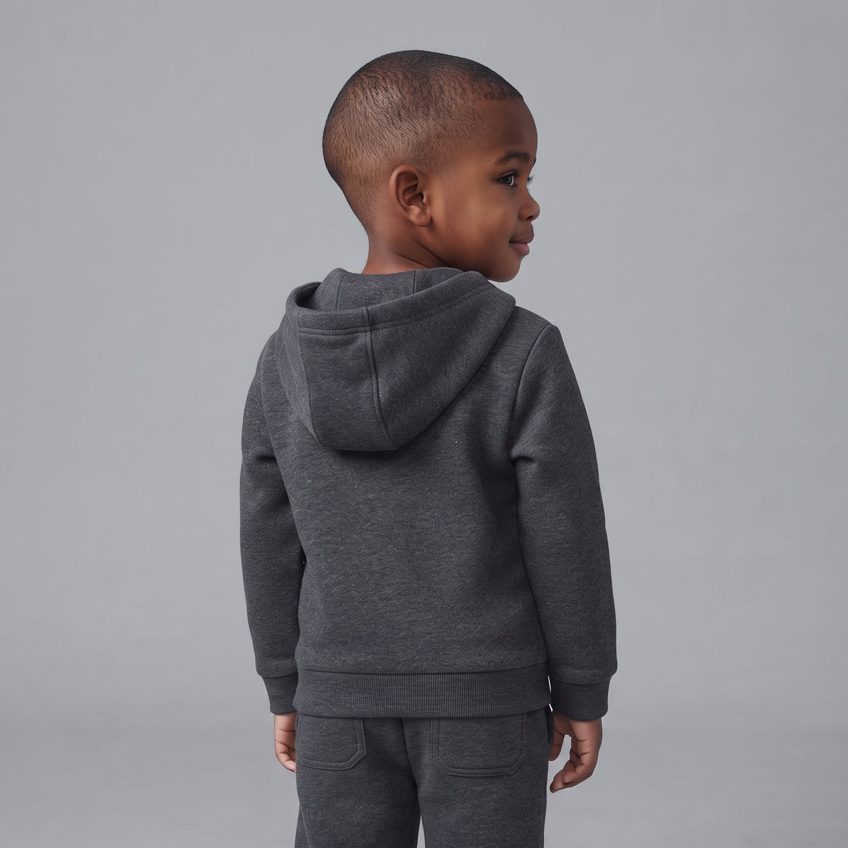 Niño de espaldas vistiendo sudadera con capucha y pantalón jogger gris oscuro de EmpiBy con temática de Disney