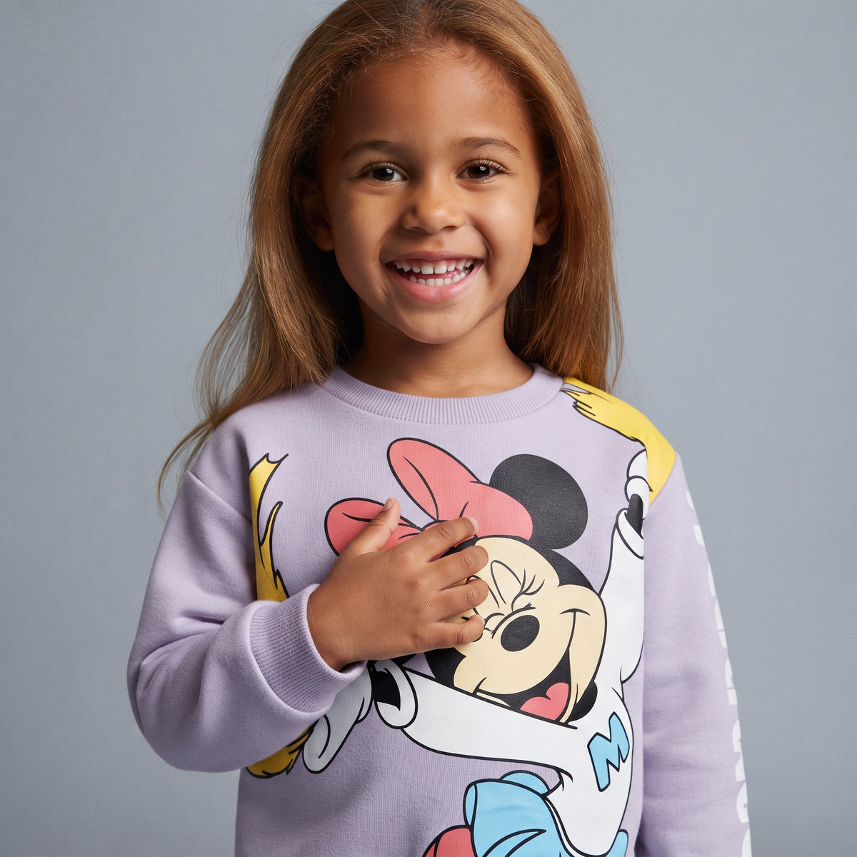 Niña sonriente vistiendo sudadera EmpiBy lila con estampado de Minnie Mouse en tonos pastel, estilo casual y cómodo.