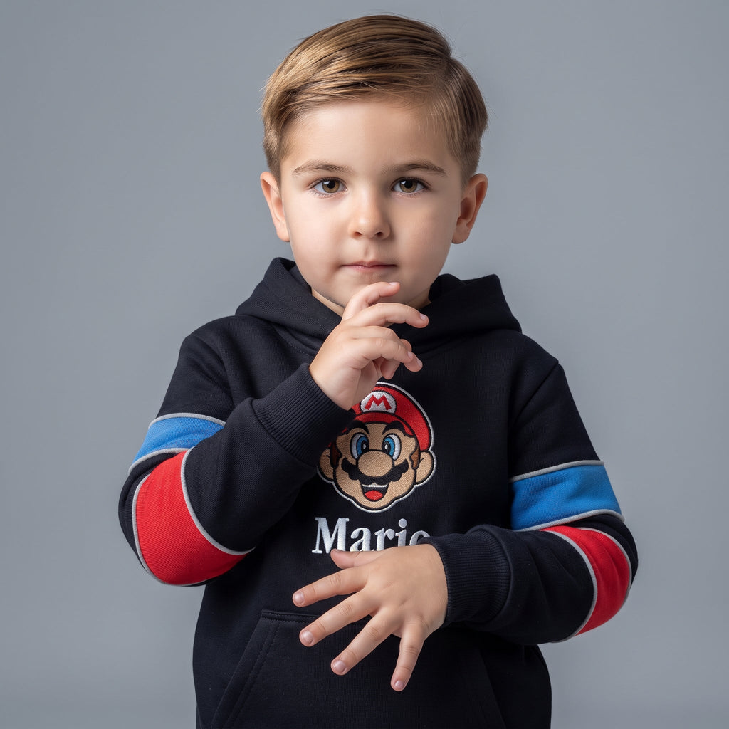 Niño vistiendo sudadera negra con capucha EmpiBy de Mario Bros con detalles en rojo y azul sobre fondo gris