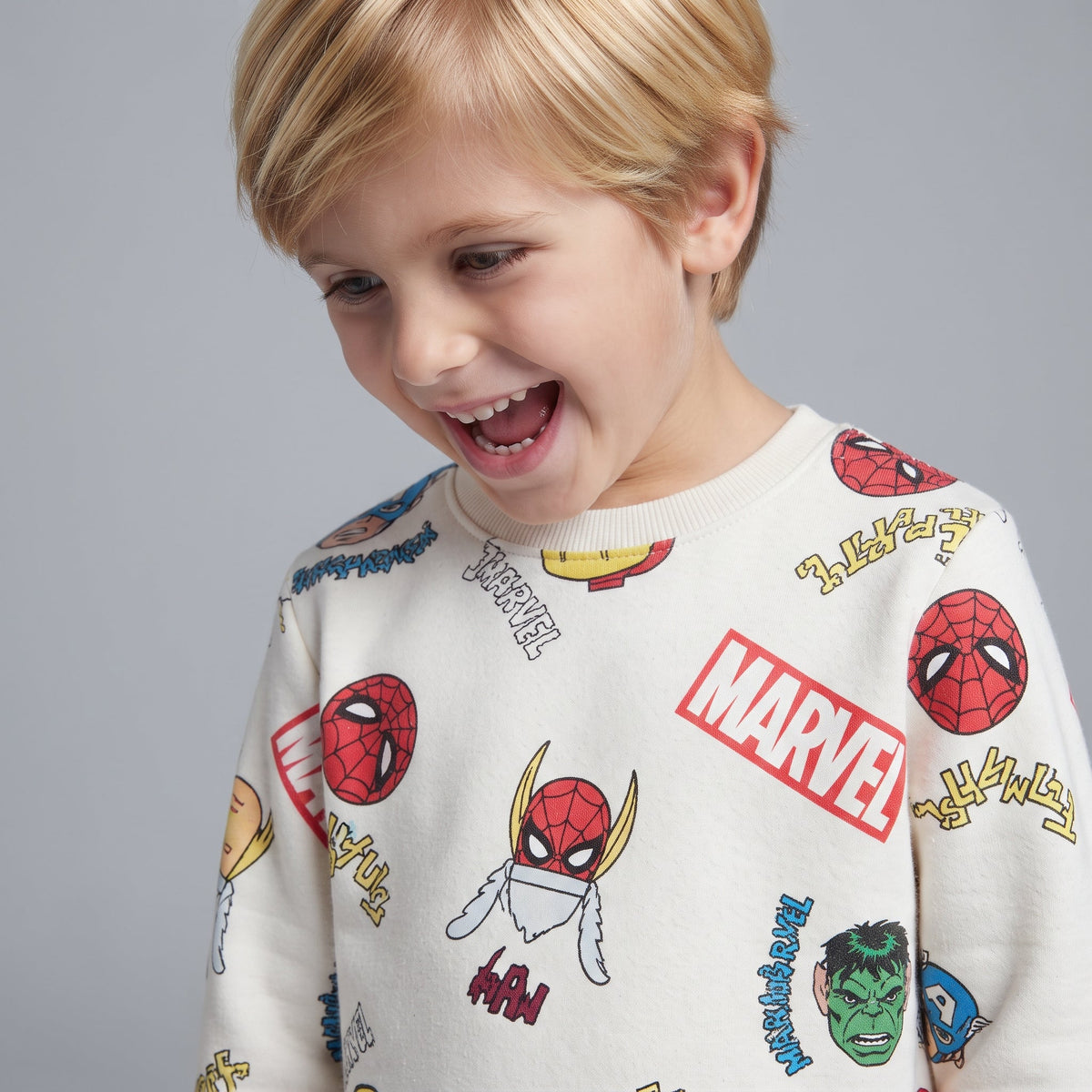 Niño sonriente vistiendo sudadera EmpiBy de color marfil con estampado colorido de superhéroes de Marvel